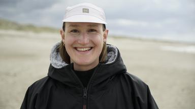 Fabienne Schwerzmann steht am Strand und schaut lächelnd in die Kamera.