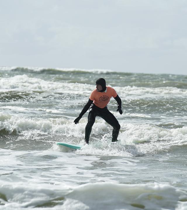 Ein Surfer steht auf dem offenen Meer in Dänemark auf seinem Surfbrett.