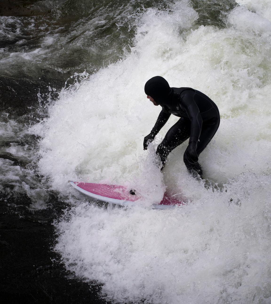 Ein Mann surft mit seinem Board auf der provisorischen Eisbachwelle im Englischen Garten.
