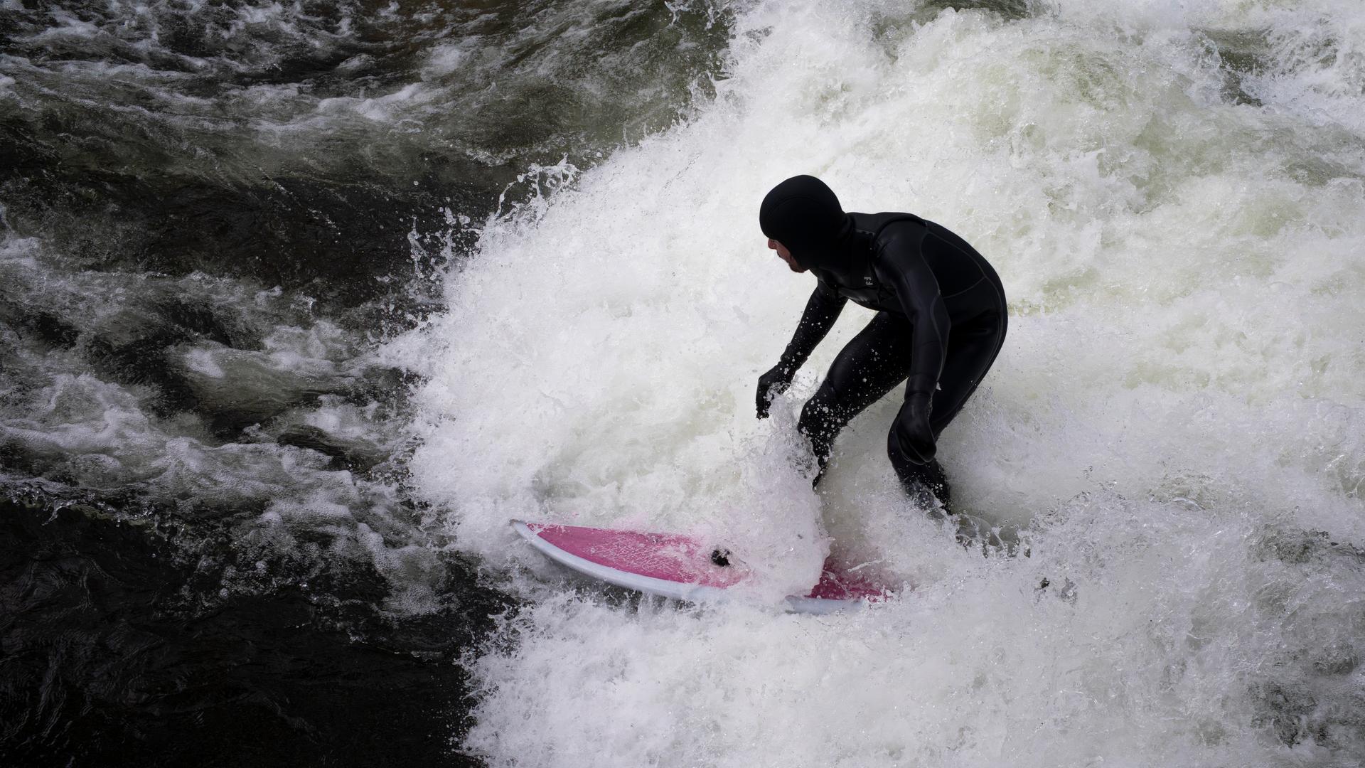 Ein Mann surft mit seinem Board auf der provisorischen Eisbachwelle im Englischen Garten.