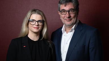 Susanne Schubert und Stefan Hartmann stehen vor einem roten Hintergrund