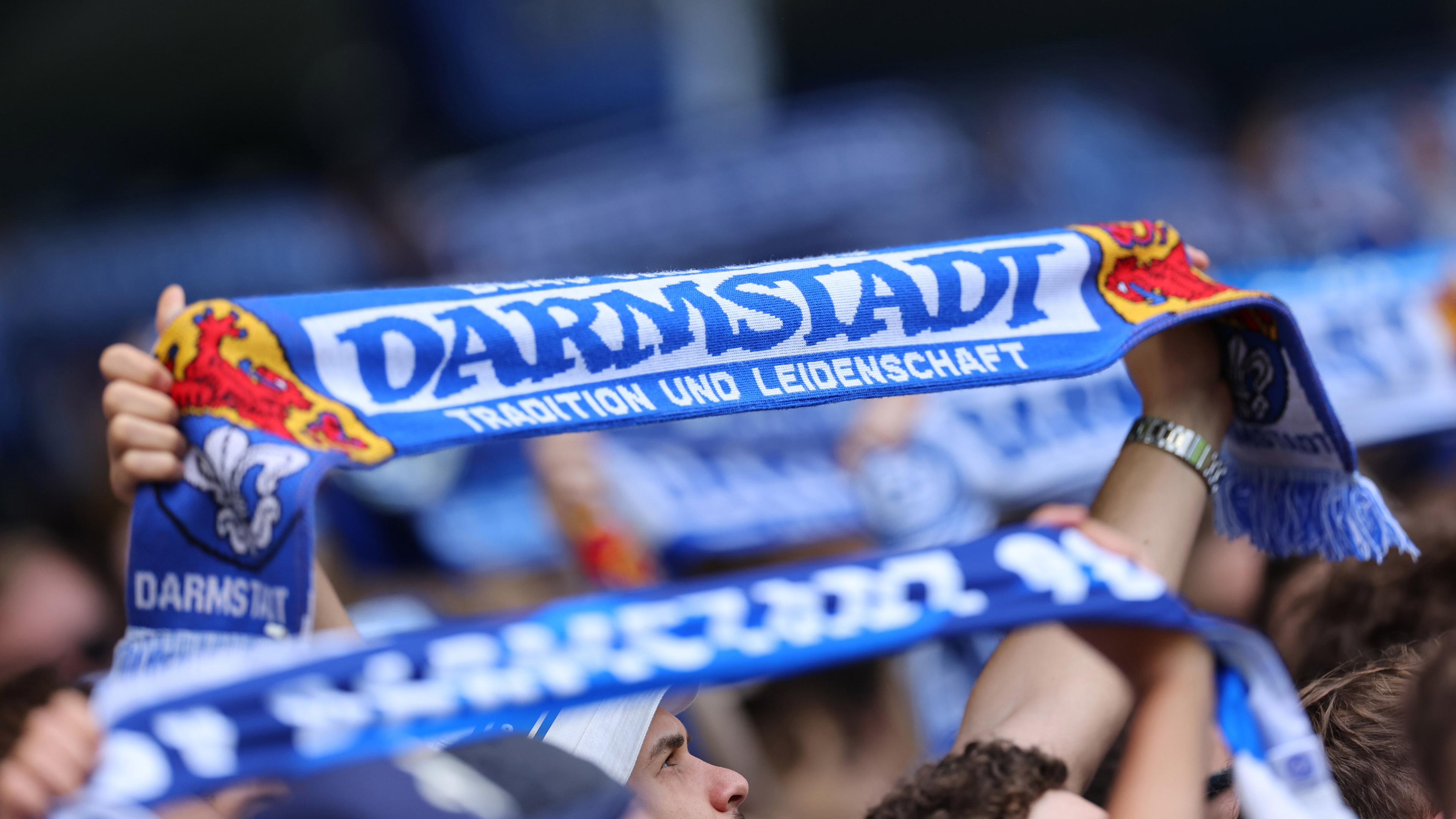 Darmstadt 98 Fans in blau halten bei einem Fußballspiel blaue Schals hoch.