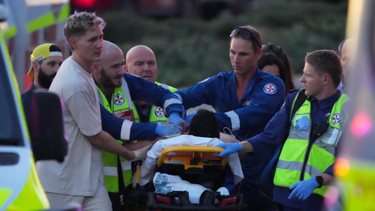 14.12.2025, Australien, Sydney: Rettungskräfte transportieren eine Person auf einer Bahre nach einem Zwischenfall am Bondi Beach in Sydney.