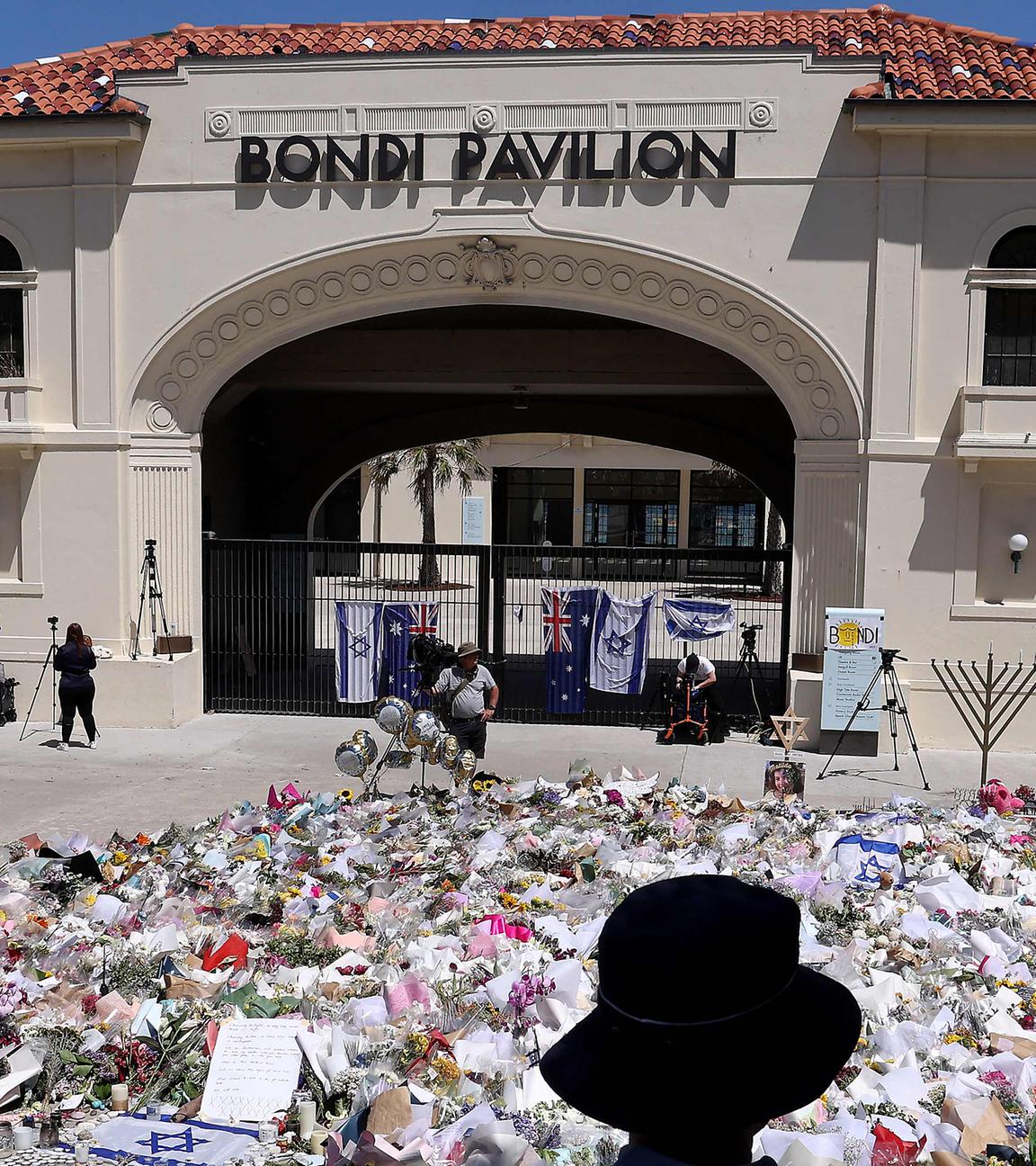 Trauernde stehen in Sydney neben aufgetürmten Gedenkgegenständen vor dem Bondi Pavilion, aufgenommen am 17.12.2025