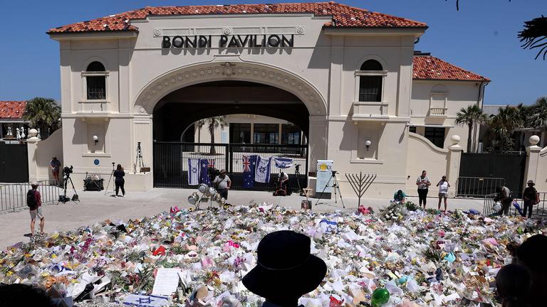 Trauernde stehen in Sydney neben aufgetürmten Gedenkgegenständen vor dem Bondi Pavilion, aufgenommen am 17.12.2025