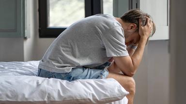 Ein Mann sitzt niedergeschlagen auf einer Bettkante. (Symbolbild)