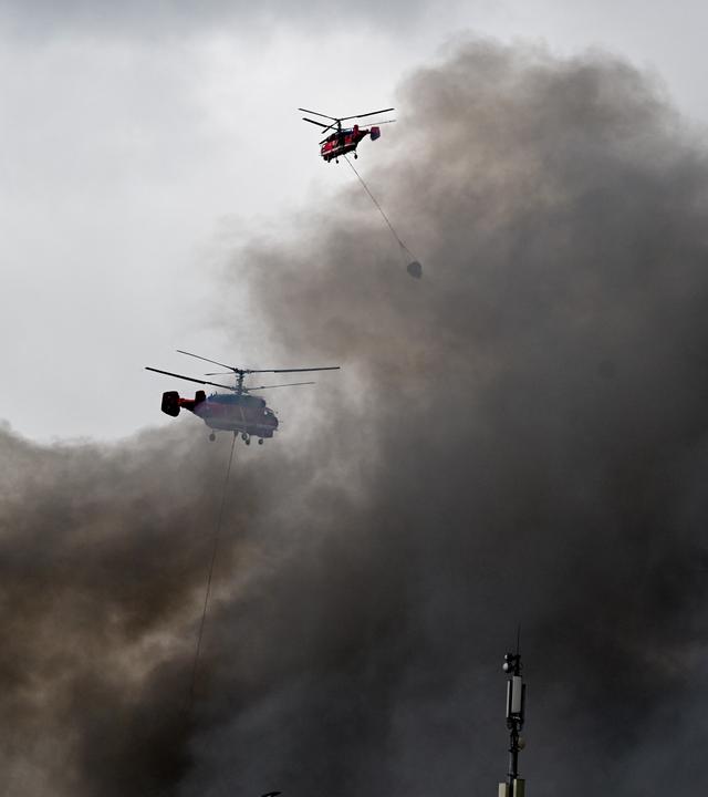 Zwei Hubschrauber fliegen über dem Rauch einer brennenden Ölraffinerie. (Symbolbild)