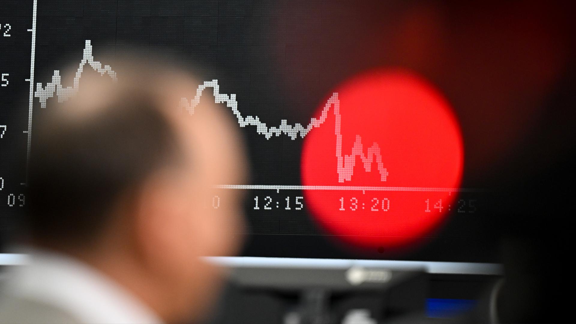 (Archiv) Börsenjournalist steht bei der Aufzeichnung eines Interviews auf dem Parkett der Frankfurter Wertpapierbörse vor der Anzeigetafel mit der Dax-Kurve.