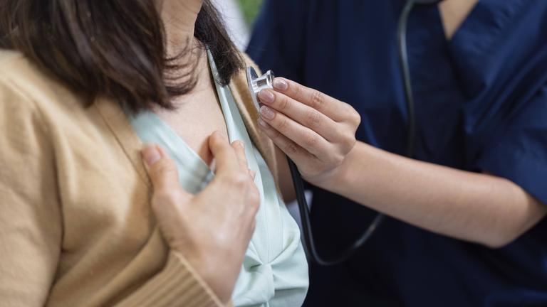 Eine Pflegekraft hört mit einem Stethoskop sorgfältig das Herz eines Patienten ab.