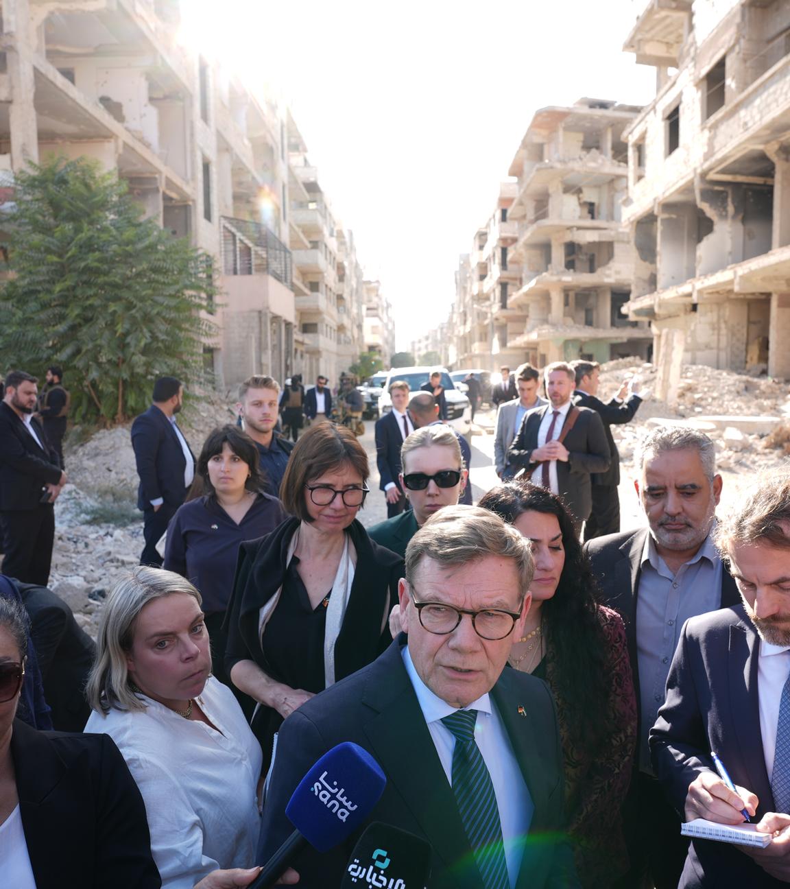 Johann Wadephul (M, CDU), Bundesminister des Auswärtigen, steht vor einer Straße mit während des Bürgerkriegs zerbombten Häusern.