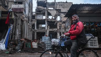 Ein Mann radelt an einem Gebäude vorbei, das durch Luftangriffe während der Assad-Herrschaft in Douma, am Stadtrand von Damaskus, beschädigt wurde.