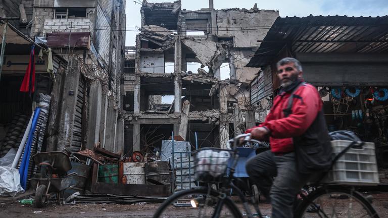 Ein Mann radelt an einem Gebäude vorbei, das durch Luftangriffe während der Assad-Herrschaft in Douma, am Stadtrand von Damaskus, beschädigt wurde.