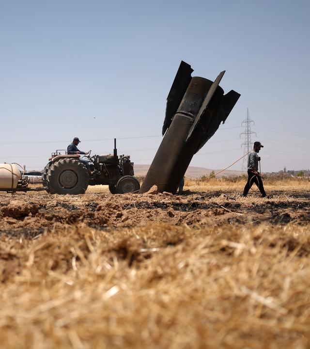 Menschen im syrischen Najha arbeiten auf einem Feld neben den Überresten einer israelischen Raketen.