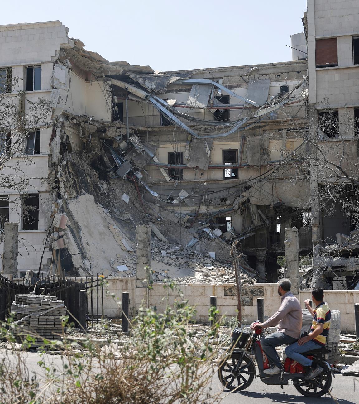 People pass in front the Syrian Defense Ministry building which on Wednesday was heavily damaged by Israeli airstrikes in Damascus, Syria, Thursday, July 17, 2025.