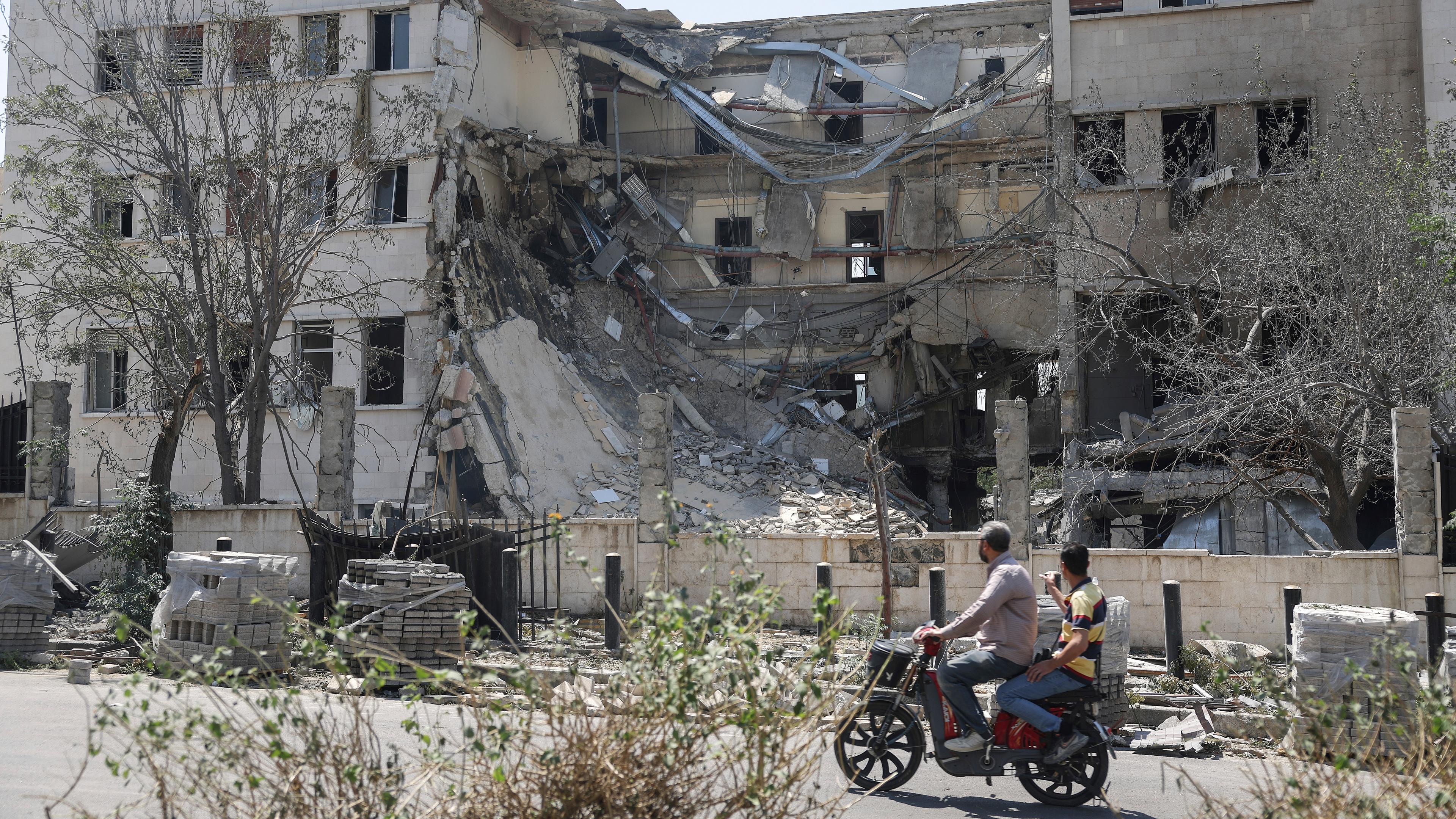 People pass in front the Syrian Defense Ministry building which on Wednesday was heavily damaged by Israeli airstrikes in Damascus, Syria, Thursday, July 17, 2025.