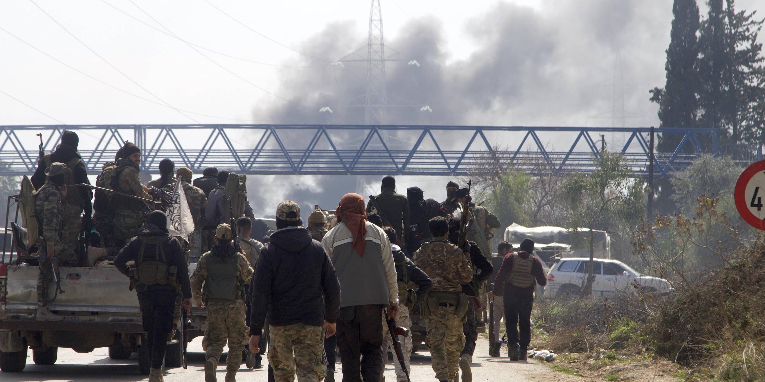 Syrische Sicherheitskräfte laufen auf der Schnellstraße zwischen Tartous und Latakia, im Norden Syriens, im Hintergrund steigt Rauch auf.
