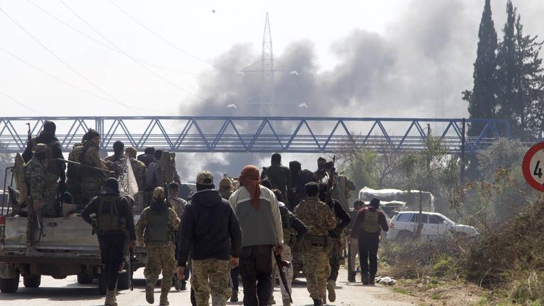 Syrische Sicherheitskräfte laufen auf der Schnellstraße zwischen Tartous und Latakia, im Norden Syriens, im Hintergrund steigt Rauch auf.