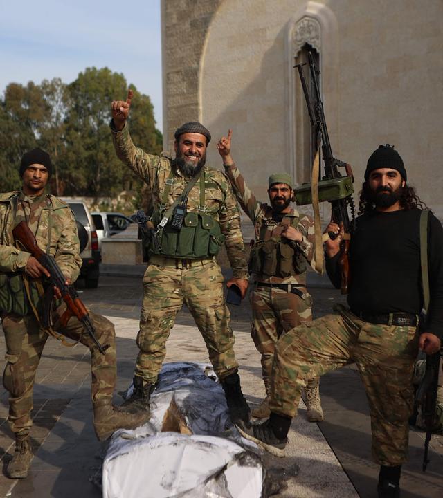 Rebel fighters pose for a picture outside the mausoleum of Syria's late president Hafez al-Assad in the family's ancestral village of Qardaha in the western Latakia province on December 11, 2024, after it was stormed by opposition factions and his gravesite set ablaze