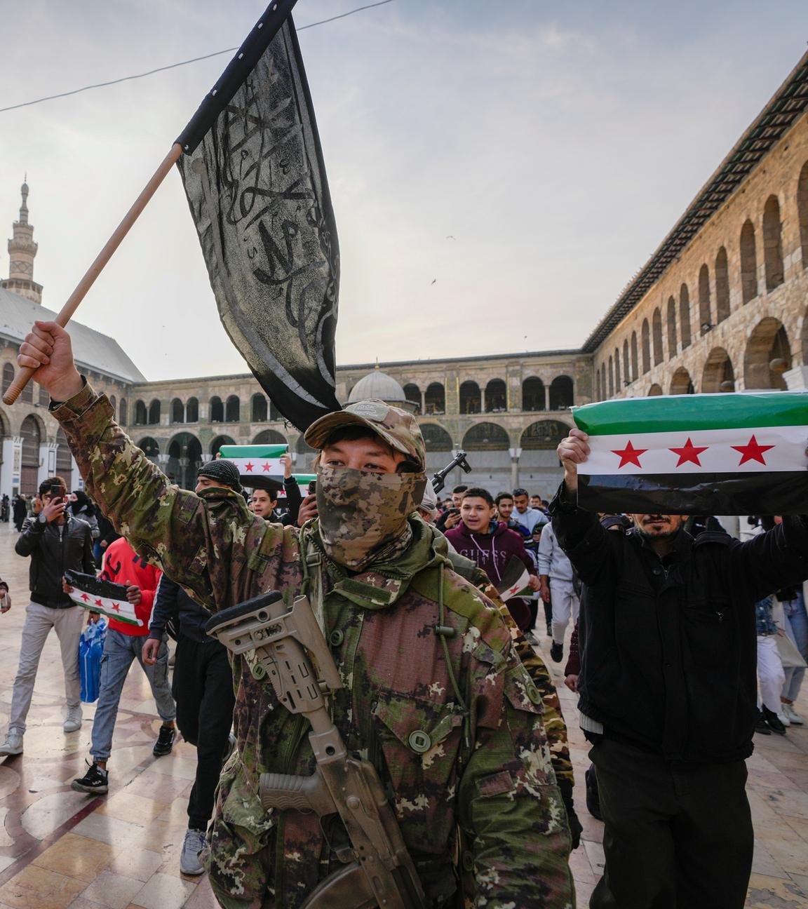 A masked opposition fighter carries a flag of Hayat Tahrir al-Sham (HTS) in the courtyard of the Umayyad Mosque in the old walled city of Damascus, Syria, on Tuesday, Dec. 10, 2024. HTS is the largest rebel faction within the opposition that toppled Bashar Assad's regime last Sunday. (AP Photo/Hussein Malla)