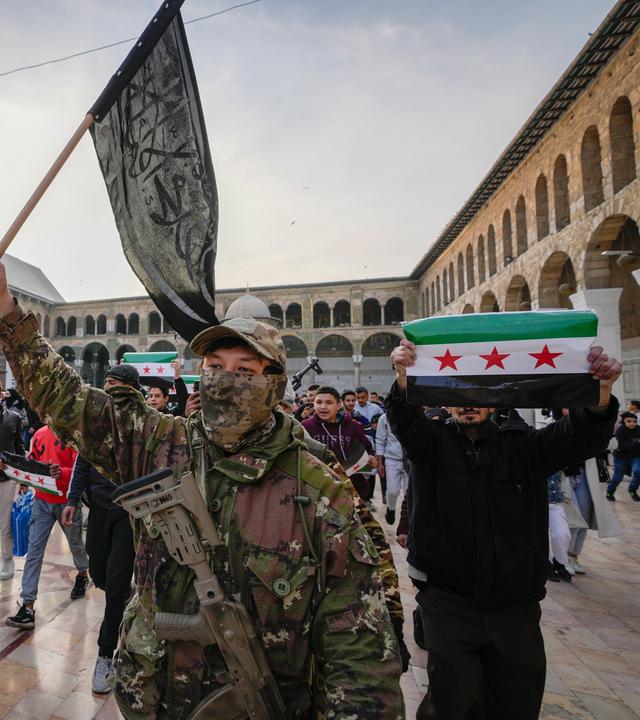 A masked opposition fighter carries a flag of Hayat Tahrir al-Sham (HTS) in the courtyard of the Umayyad Mosque in the old walled city of Damascus, Syria, on Tuesday, Dec. 10, 2024. HTS is the largest rebel faction within the opposition that toppled Bashar Assad's regime last Sunday. (AP Photo/Hussein Malla)