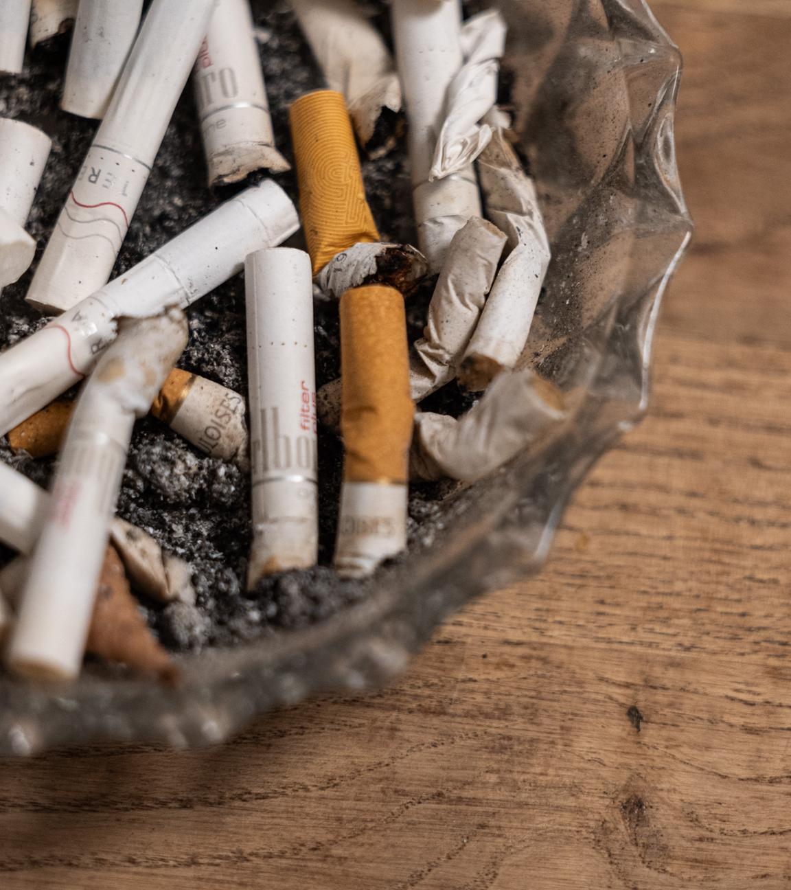 Ein Aschenbecher mit konsumierten Zigaretten und Tabaksticks steht auf einem Tisch.