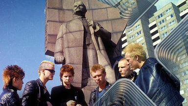 Sechs junge Punks mit kurzgeschorenen und gefärbten Haaren, gekleidet in Lederjacken, posieren vor dem Lenin-Denkmal in Ost-Berlin, 1982.