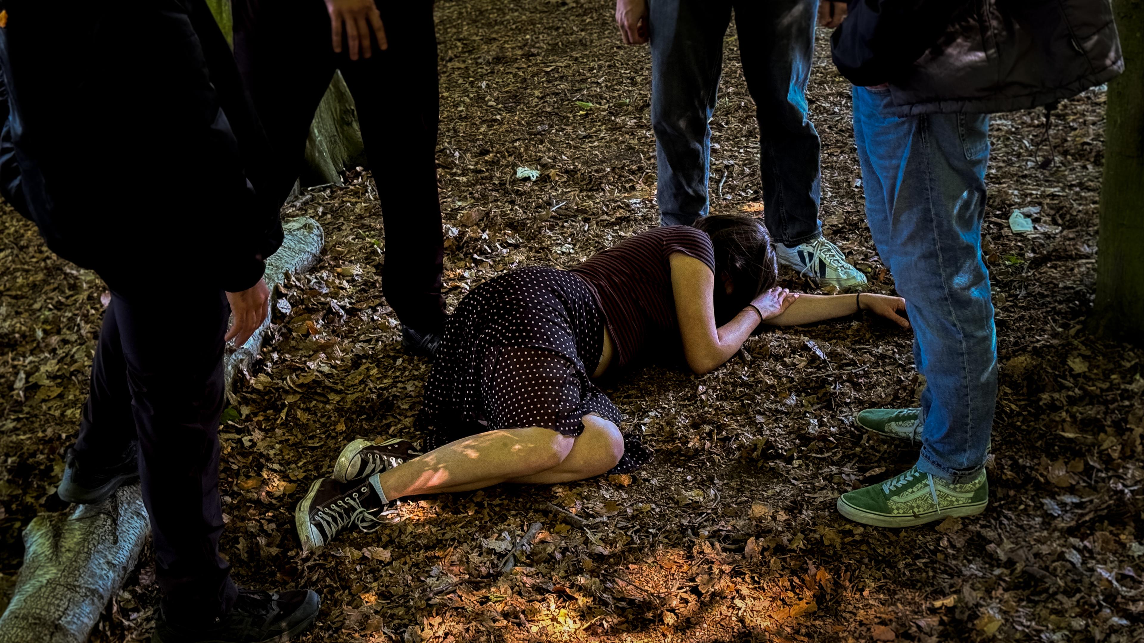 Nachgestellte Szene: Mehrere junge Männer stehen um ein Mädchen herum, das auf dem Boden im Hamburger Stadtpark liegt.