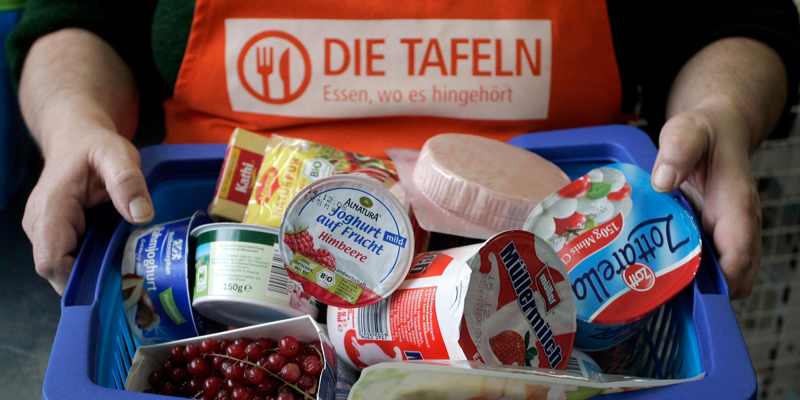 Ein Korb voller Lebensmitteln für Hilfsbedürftige. Im Hintergrund ist das Logo der Tafeln zu sehen.