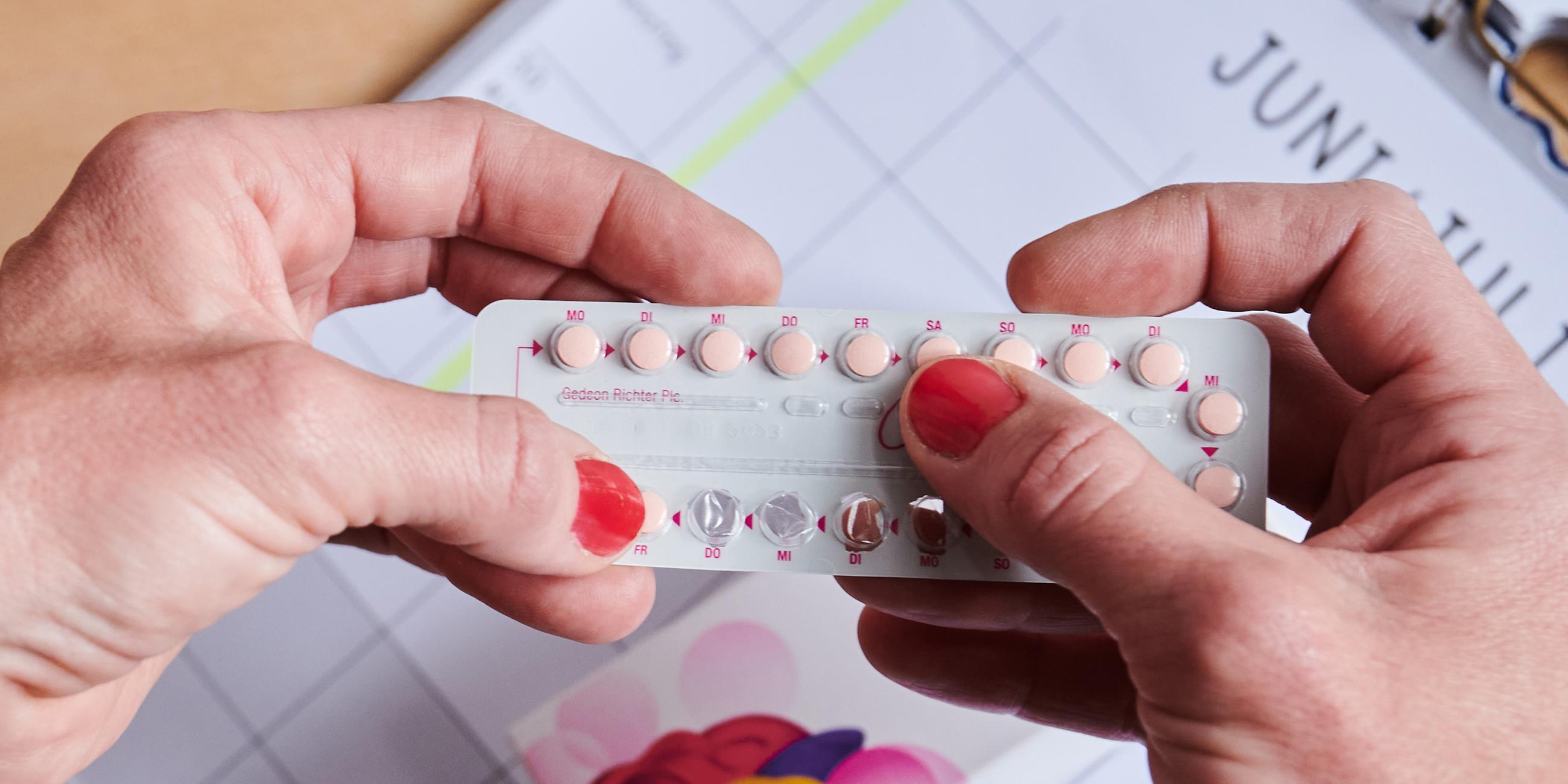  Eine teilweiße schon geöffnete Monatspackung der Antibabypille hält eine Frau in der Hand.