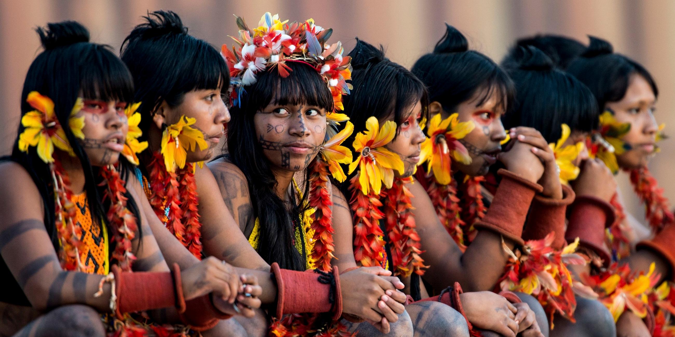 Gruppe von jungen indigenen Frauen. Sie haben sich mit Federn und Blumen geschmückt.