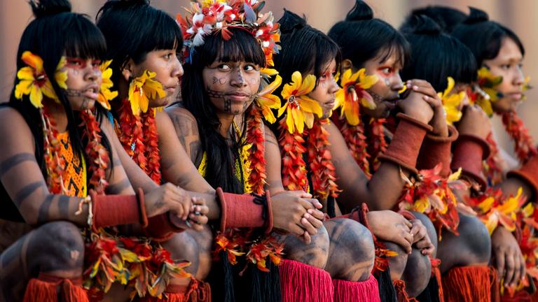 Gruppe von jungen indigenen Frauen. Sie haben sich mit Federn und Blumen geschmückt.