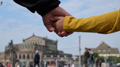 Ein Mann und ein Kind halten sich am Tag der Deutschen Einheit bei einer Menschenkette auf Schlossplatz vor der Semperoper in Dresden an den Händen.