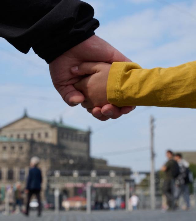 Ein Mann und ein Kind halten sich am Tag der Deutschen Einheit bei einer Menschenkette auf Schlossplatz vor der Semperoper in Dresden an den Händen.