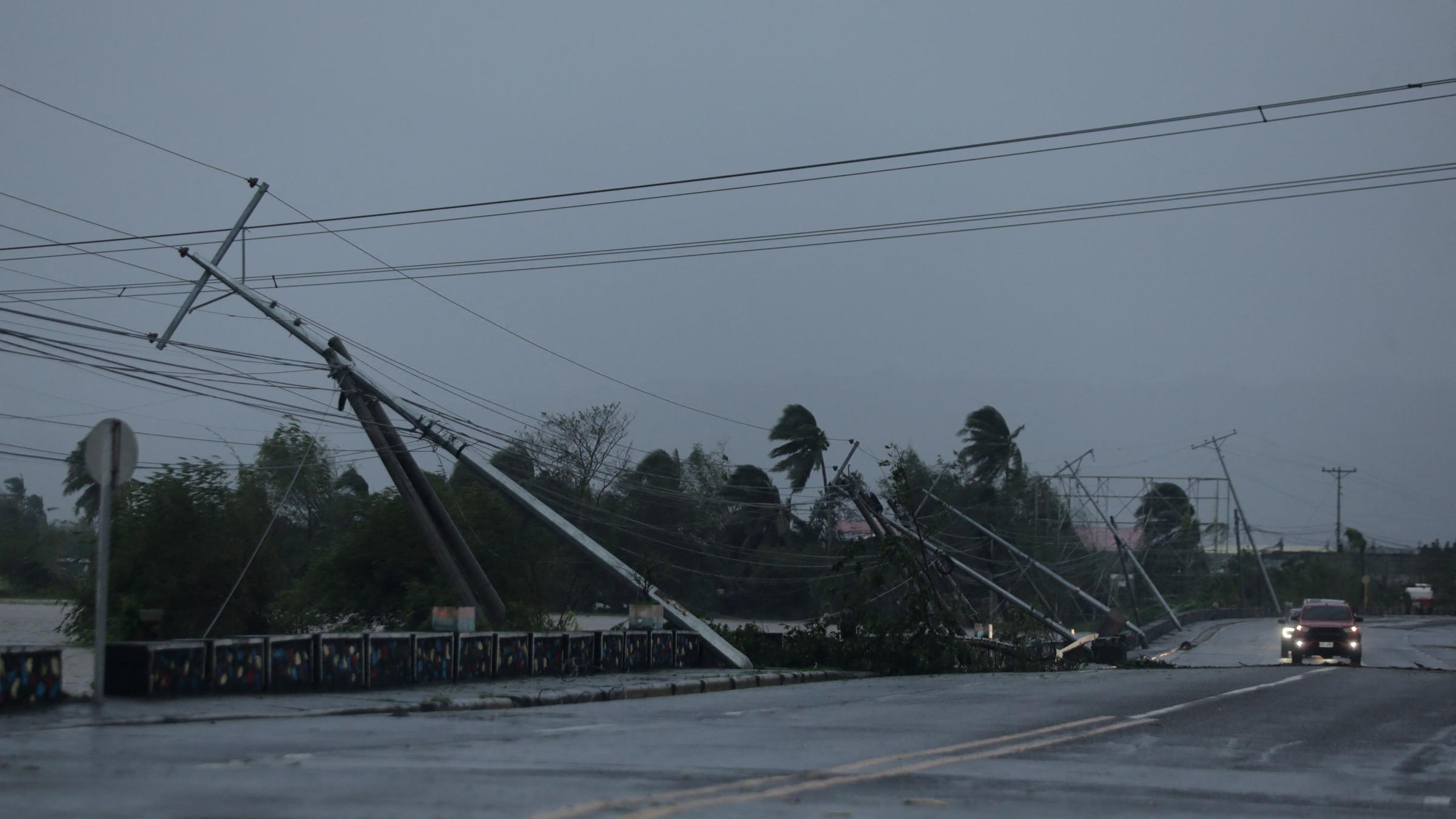 Fahrzeuge rasen am 09.11.2025 an beschädigten Strommasten entlang einer Autobahn in Polangui in der Provinz Albay südlich von Manila vorbei, nachdem der Supertaifun Fung-wong auf Land getroffen war. 