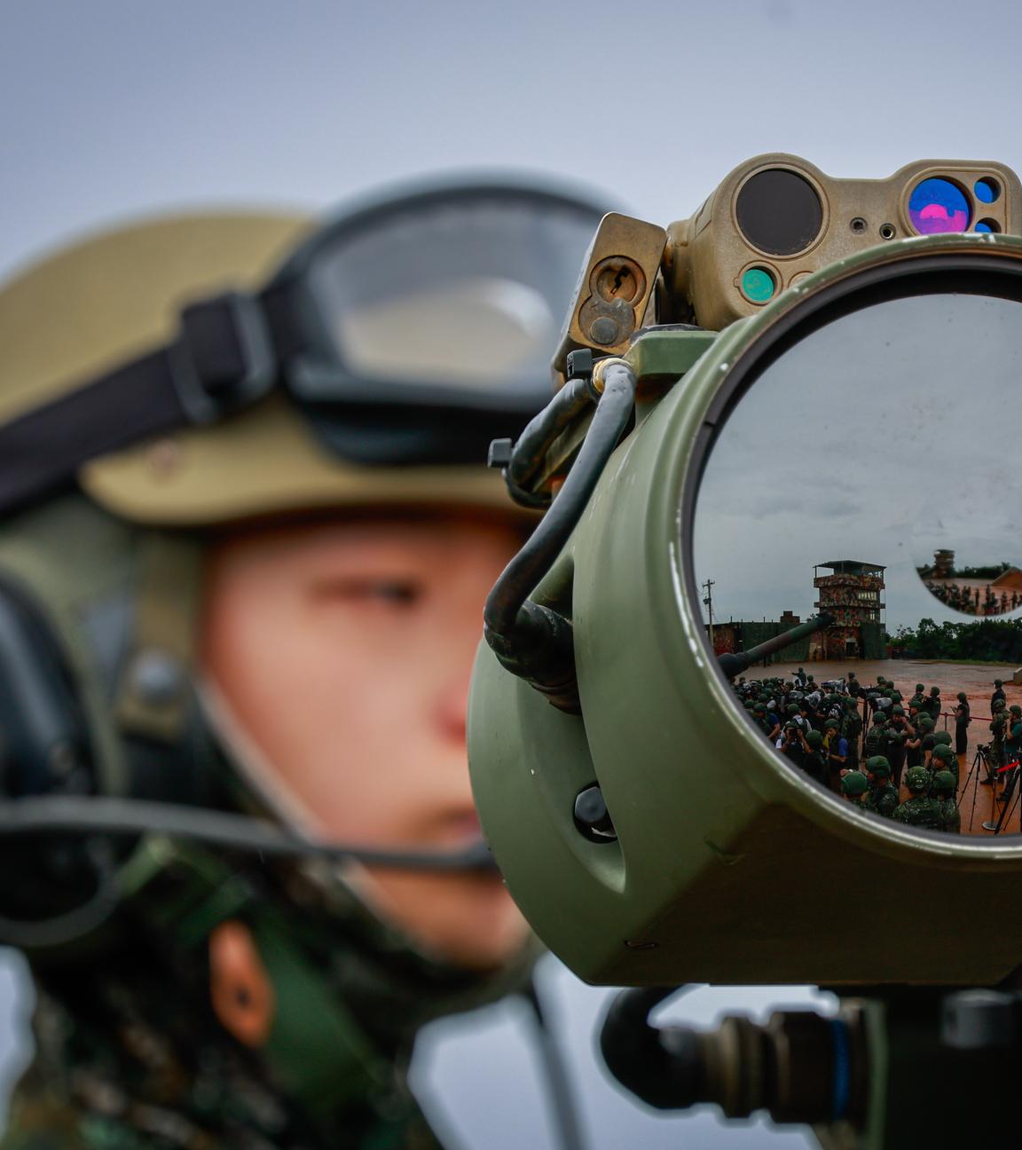 Ein taiwanesischer Soldat im Hintergrund, im Vordergrund eine große Linse, in der sich zahlreiche weitere Soldaten spiegeln.