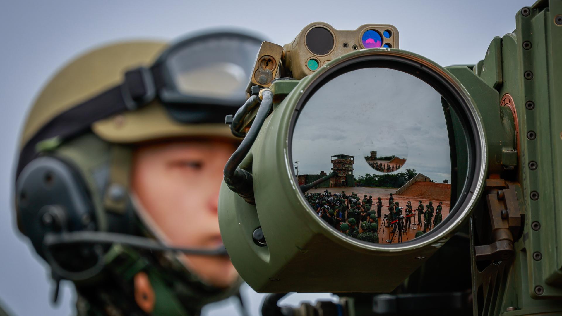 Ein taiwanesischer Soldat im Hintergrund, im Vordergrund eine große Linse, in der sich zahlreiche weitere Soldaten spiegeln.