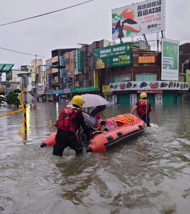 Feuerwehrleute in Taiwan, die mit einem aufblasbaren Rettungsboot Bewohner durch Hochwasser evakuieren