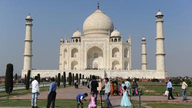 Das Taj Mahal steht vor wolkenfreiem Himmel. Menschen befinden sich auf dem Gelände.