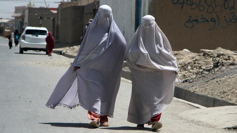 Zwei Frauen laufen in Afghanistan auf einer Straße.