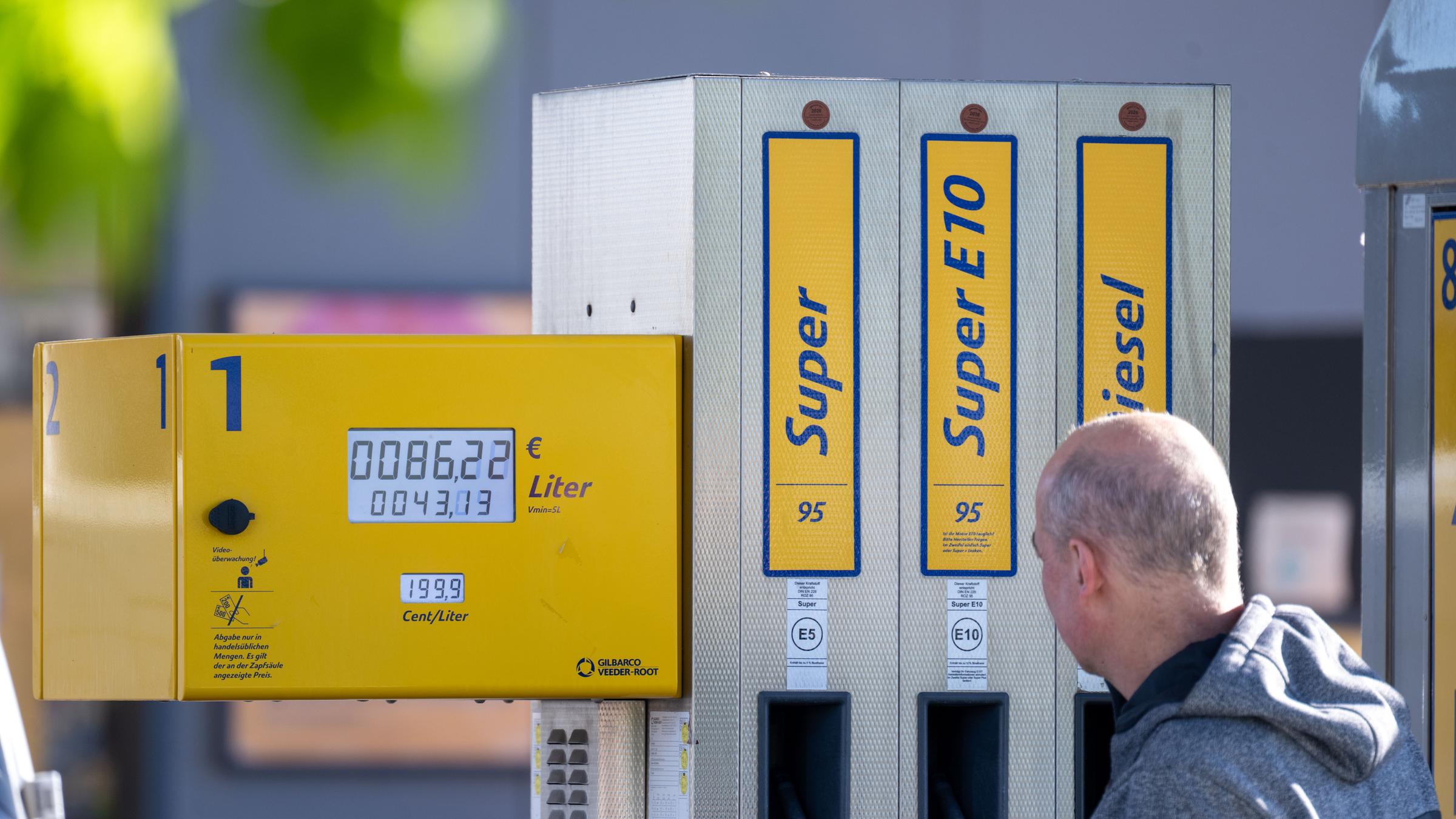 EIn Kunde steht mit seinem Auto an einer Zapfsäule, auf der steht "Super", "SuperE10" und "Diesel".