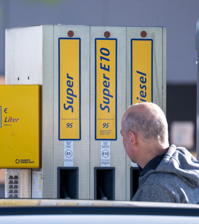 EIn Kunde steht mit seinem Auto an einer Zapfsäule, auf der steht "Super", "SuperE10" und "Diesel".