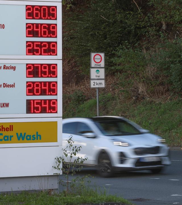 Symbolbild: Tankstelle, Stehle mit Anzeige der Spritpreise und ein fahrendes Auto