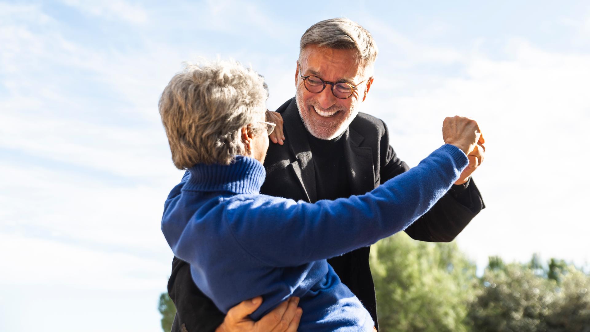 Fröhliches Seniorenpaar tanzt und umarmt sich im Garten.