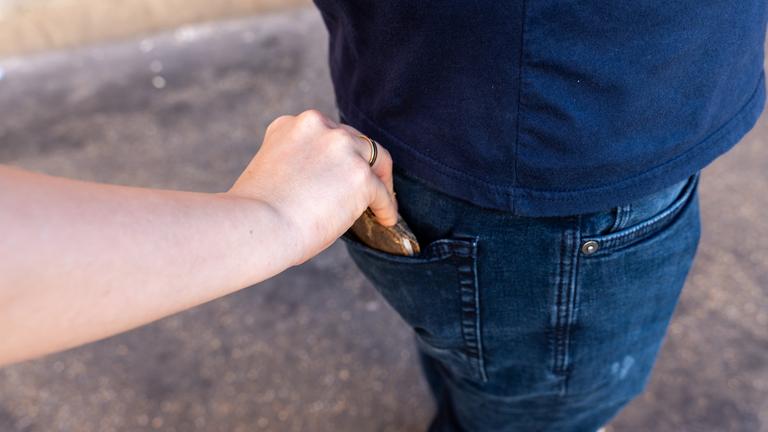 Eine Hand greift nach dem Geldbeutel in der hinteren Hosentasche eines Mannes.