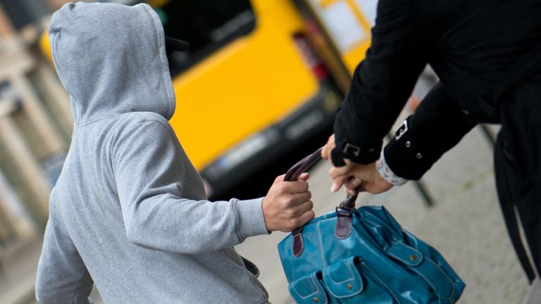 Ein Mann stiehlt einer Frau an einer Bus und Straßenbahnhaltestelle in Dresden (Sachsen) eine Handtasche.