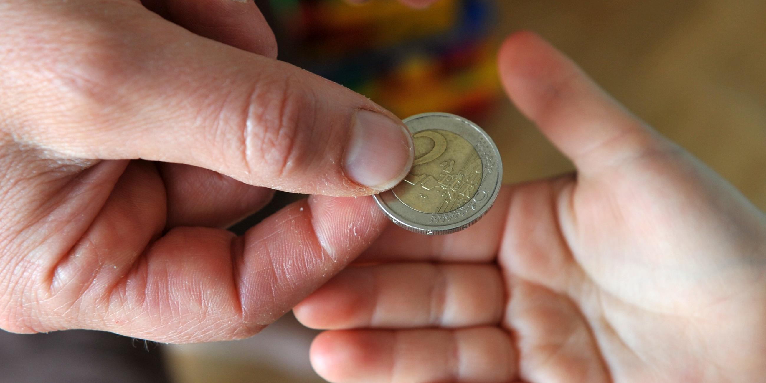 Ein Elternteil gibt dem Nachwuchs ein zwei Euro Geldstück in die Hand.