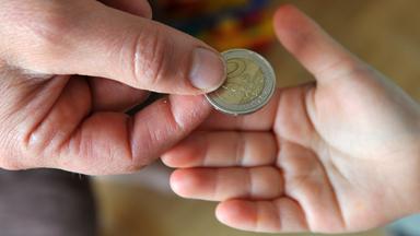 Ein Elternteil gibt dem Nachwuchs ein zwei Euro Geldstück in die Hand.