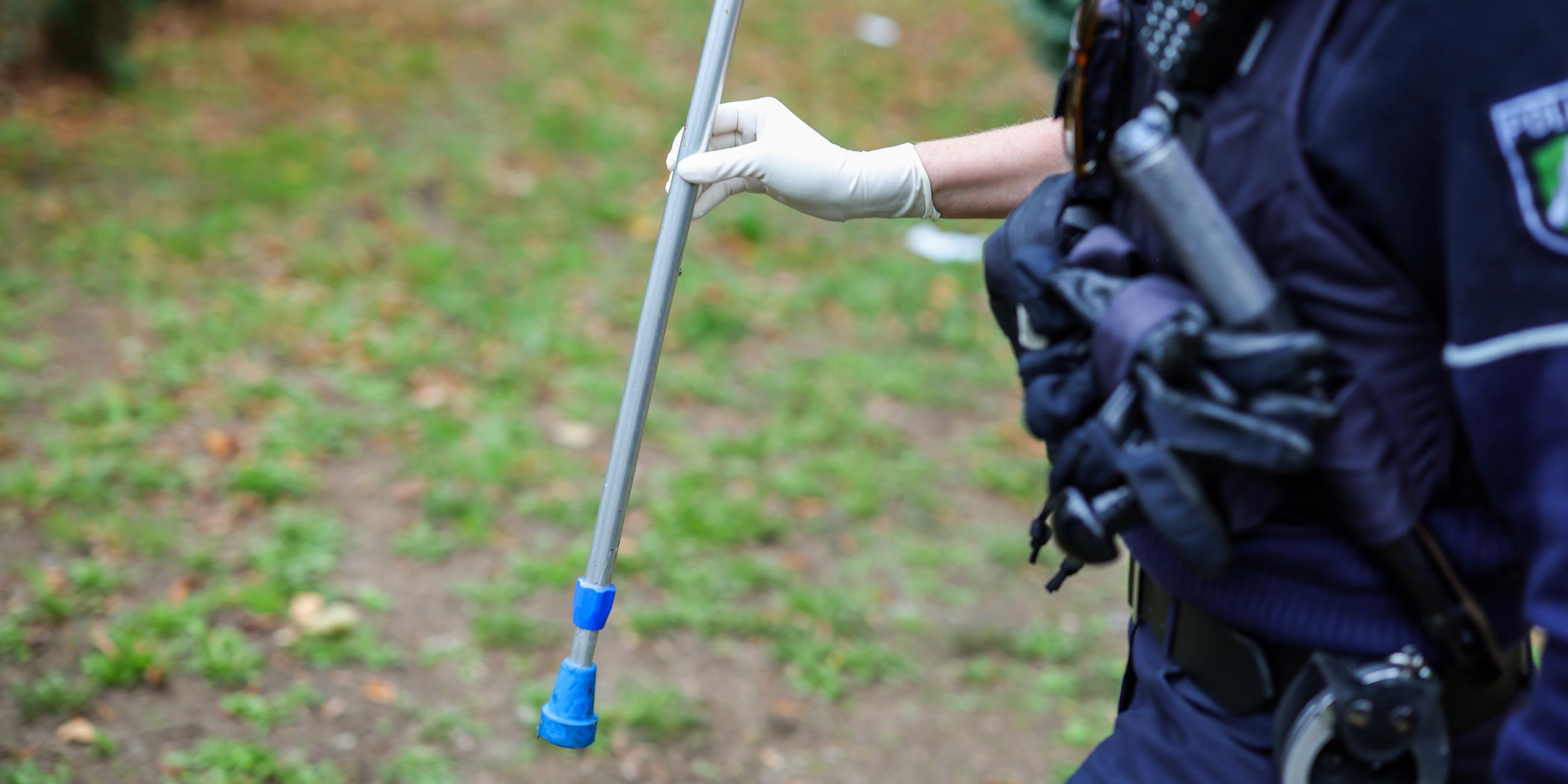  Eine Polizeibeamtin hält ein Beweismittel in der Hand, die Hälfte einer Krücke, die bei der Massenschlägerei eingesetzt worden war.