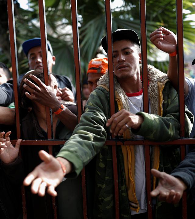 Migranten aus Mittelamerika stehen an einem Tor und stecken ihre Hände und Arme hindurch am 18.11.2018 in Tijuana.