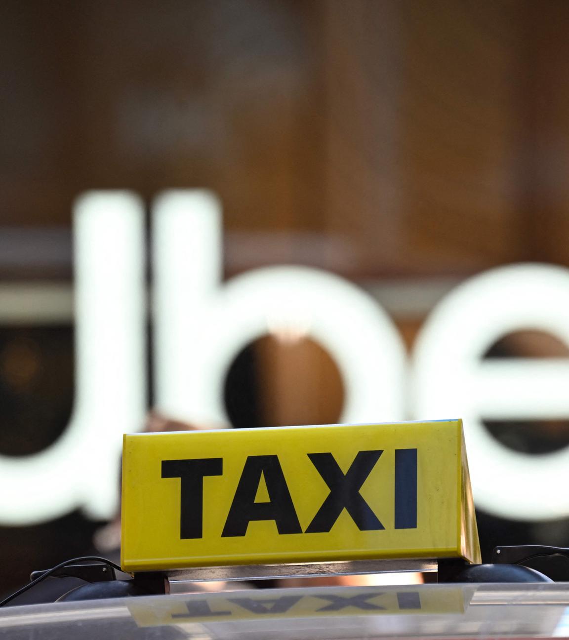 Logo eines Taxis auf einem Autodach vor dem Logo von Uber im Hintergrund